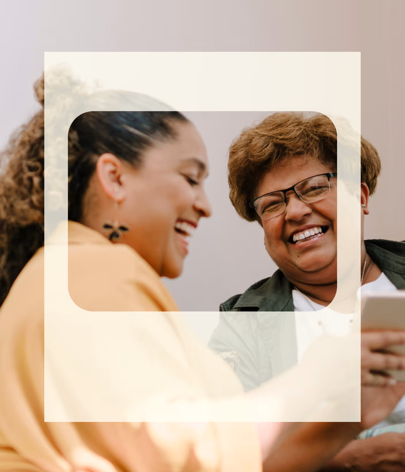 Two women smiling and laughing while looking at a smartphone.