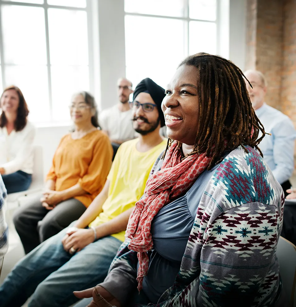 Diverse group of adults seated in a bright room, attentively listening and smiling.
