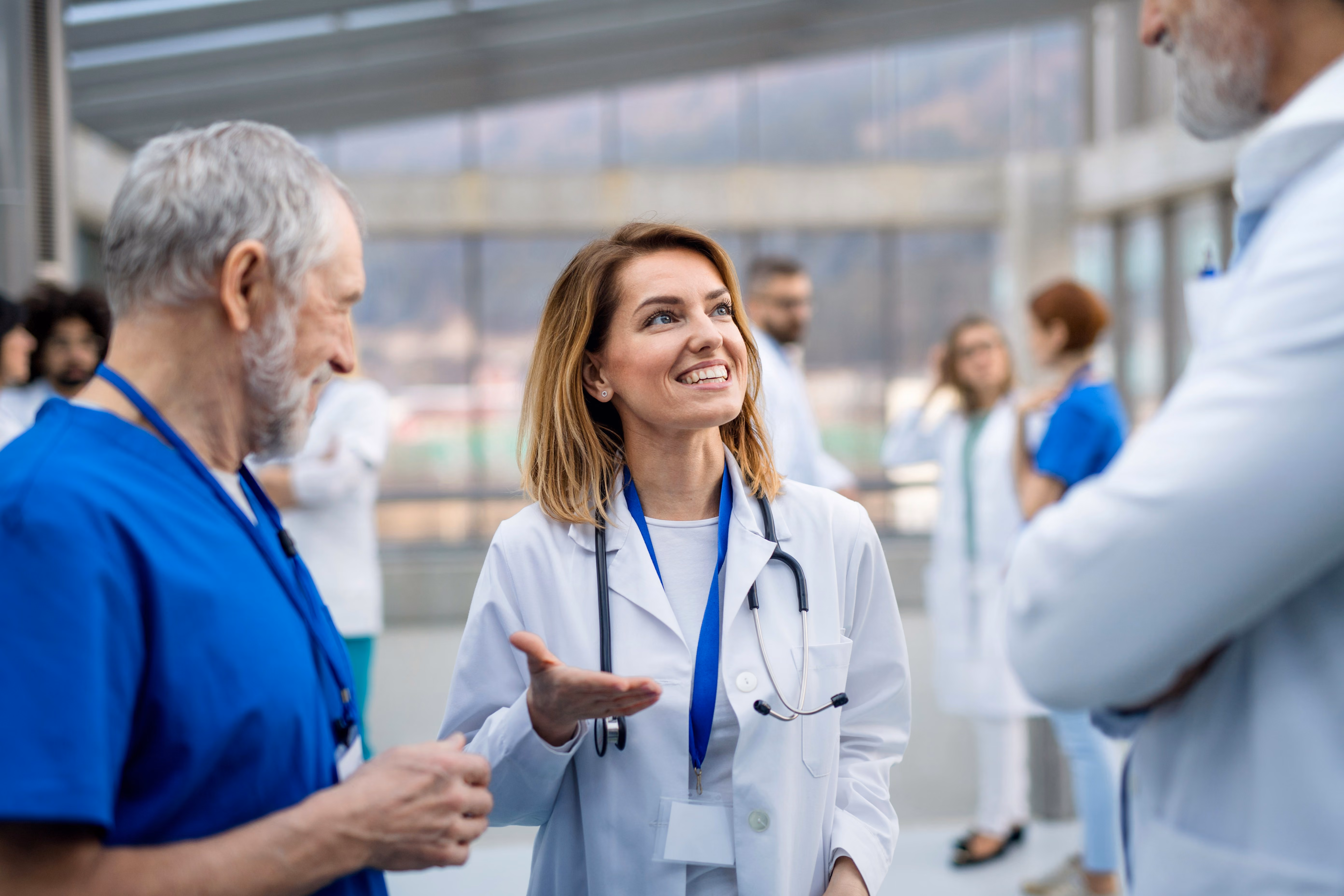 Smiling female doctor with stethoscope talking with colleagues in a modern hospital lobby.