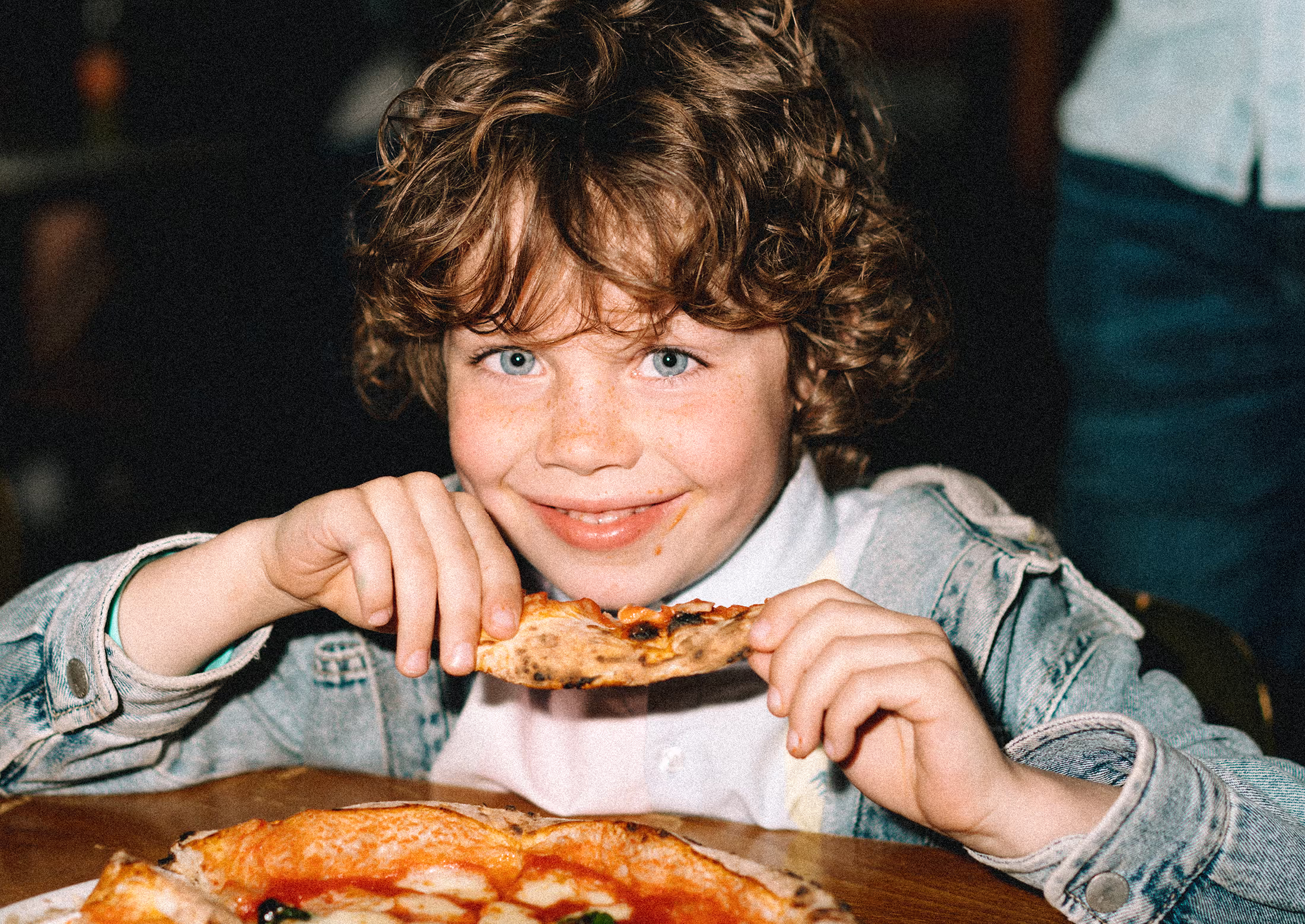 A young boy sitting at a table eating pizza.