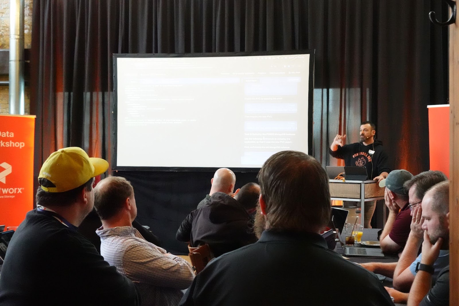 A speaker presents at a Portworx Data Workshop to an audience seated before a large projection screen.