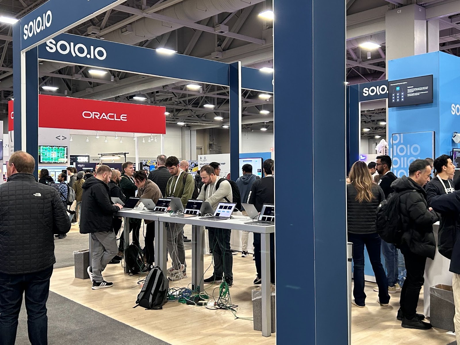 Solo.io exhibition booth at a tech conference, with attendees gathered around laptops on demo tables.