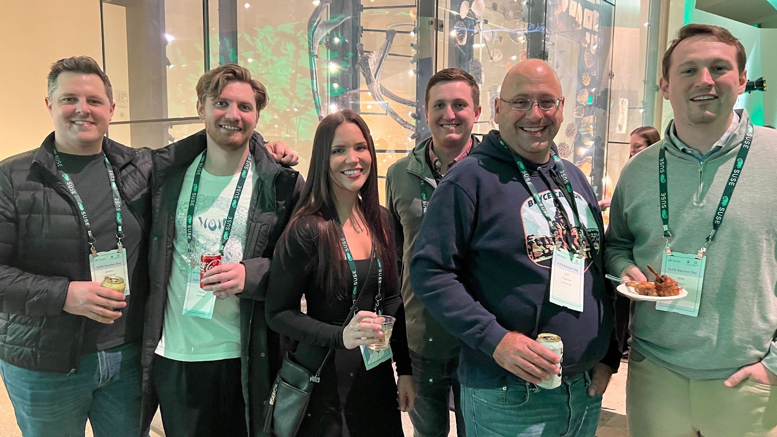 Group of attendees with SUSE Rancher Day lanyards smiling and holding drinks at a networking event.