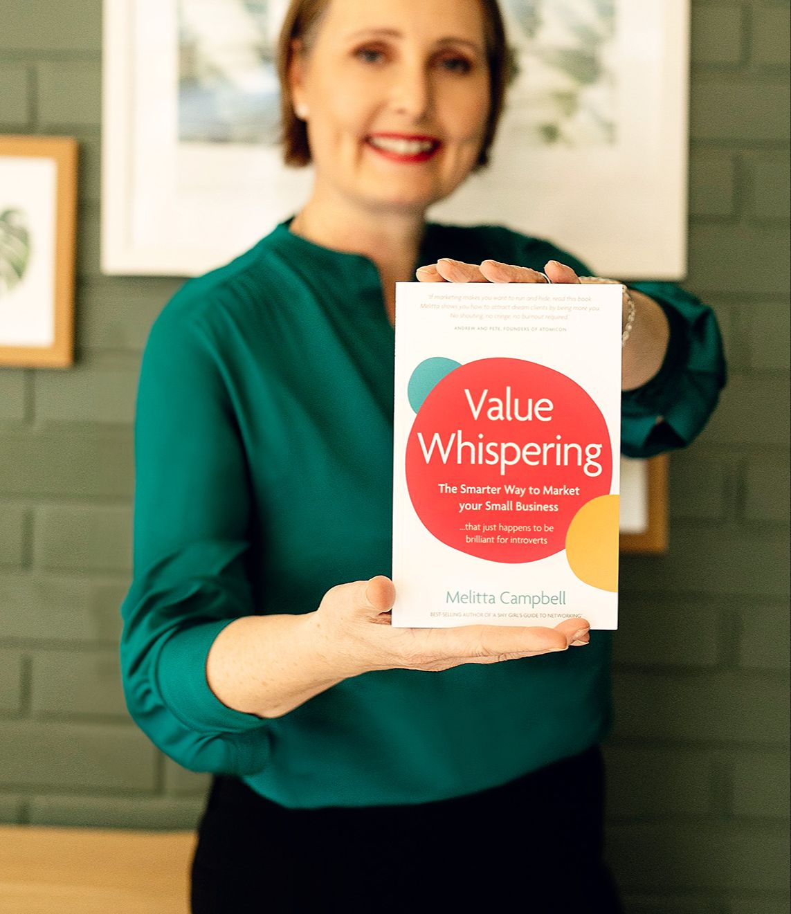 Smiling woman in green shirt holding the book 'Value Whispering' by Melitta Campbell toward the camera.