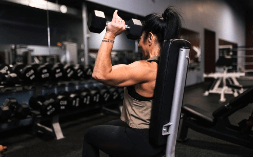 Person lifting dumbbell at gym, seated on weight machine