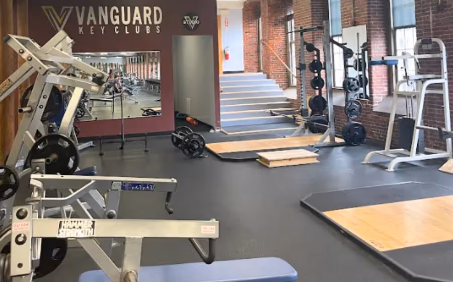 Interior of a modern gym with weight machines, squat racks, and lifting platforms.