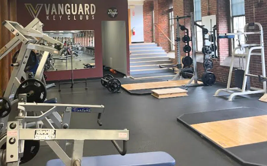 Interior of a modern gym with weight machines, squat racks, and lifting platforms.