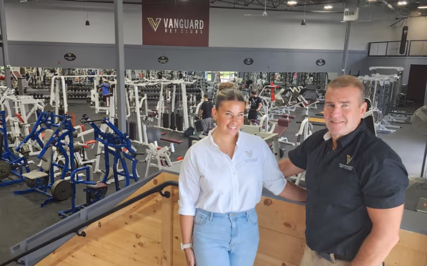 Two Vanguard Key Clubs staff members standing on an upper level overlooking a fully equipped gym floor.