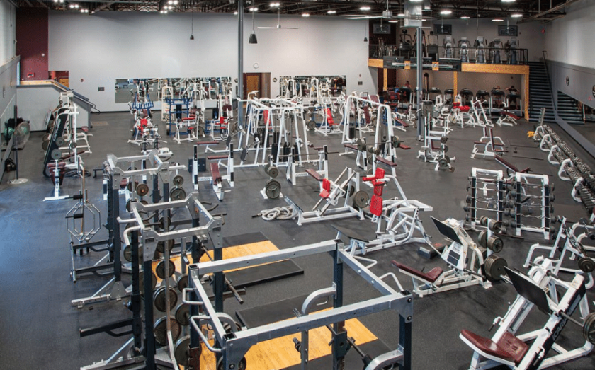 Wide view of a large gym floor filled with strength training machines, racks, and lifting platforms.