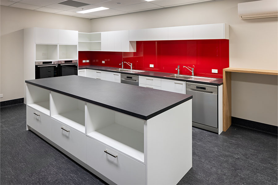 Contemporary office kitchen with red splashback and white cabinetry