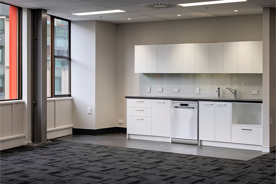 Modern kitchenette with white cabinetry and grey benchtop in office space