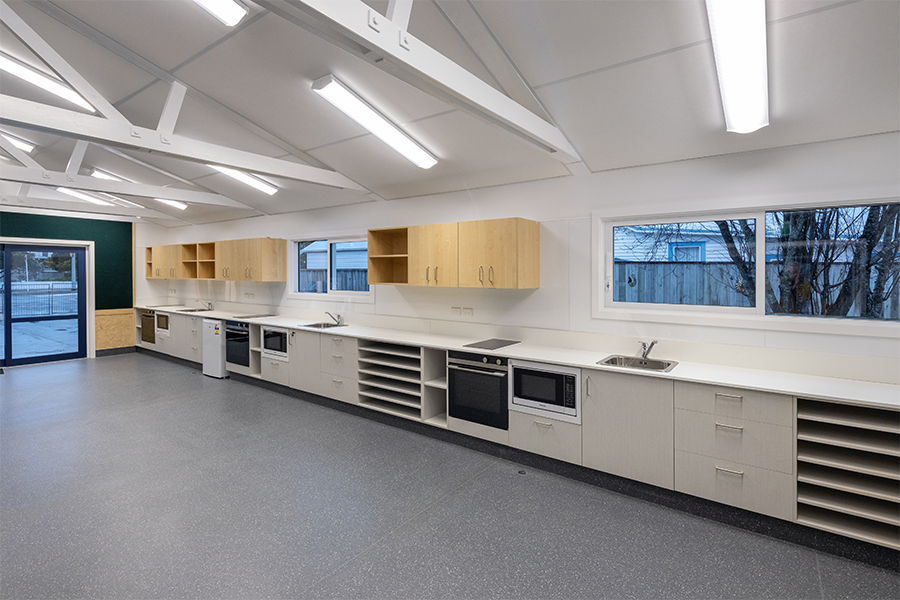 Contemporary school kitchen area with white cabinetry, ample bench space, and large windows for natural light