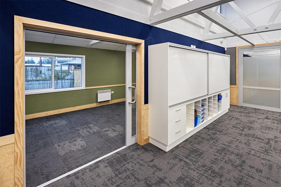 Flexible learning space with sliding doors, writable walls, and integrated cabinetry for storage.