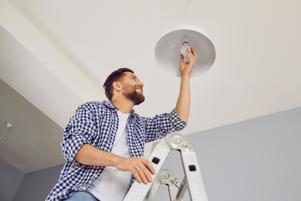Man up on a ladder changing a light bulb in his home