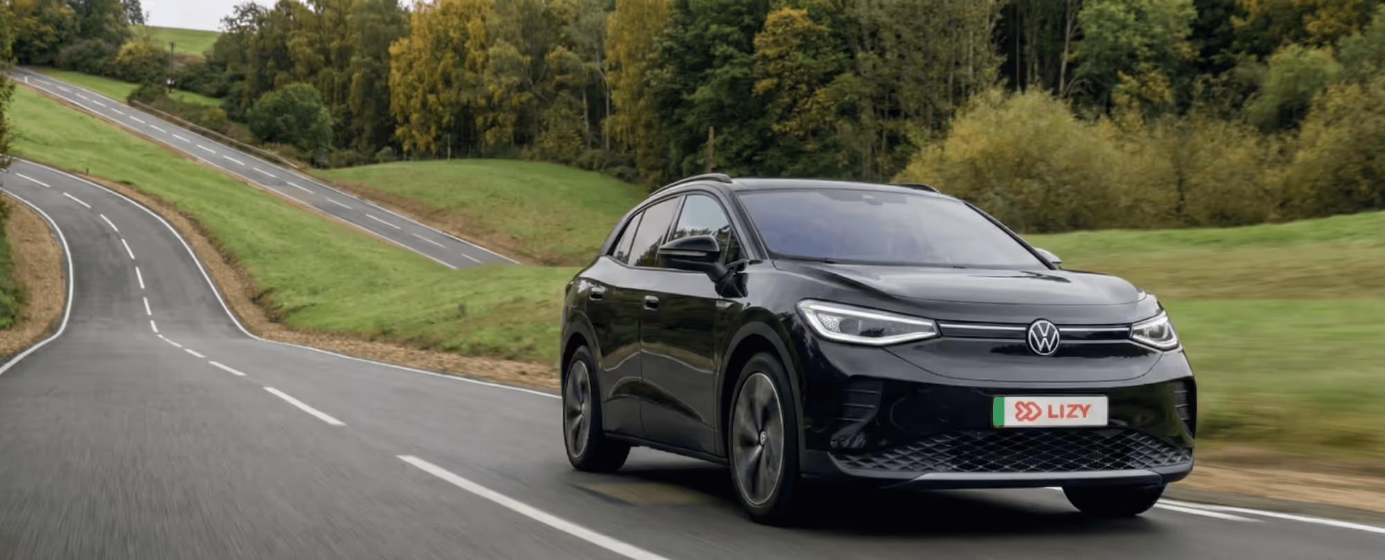 Black Volkswagen electric SUV driving on a winding road surrounded by green hills and trees.