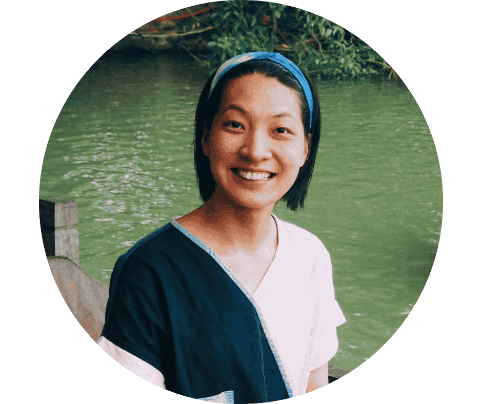 Smiling person wearing a blue headband and split-color shirt near green water outdoors.