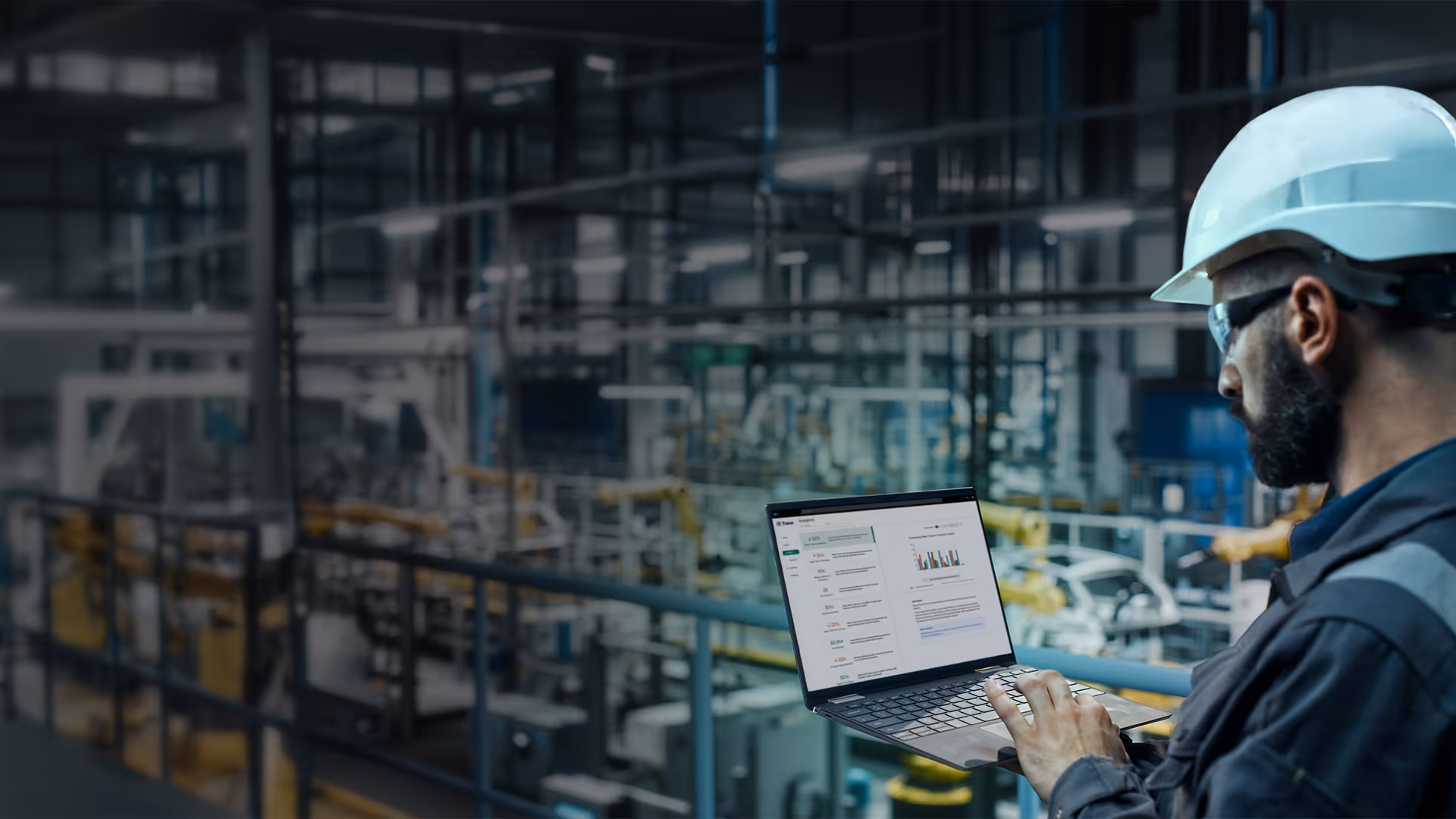Engineer wearing a white helmet and safety glasses using a laptop with data charts in an industrial factory setting.