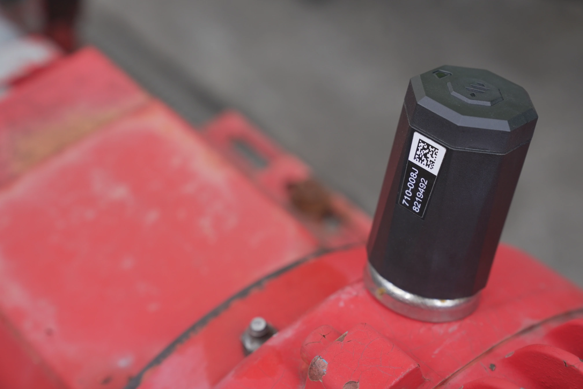 Black cylindrical sensor device with a QR code and label mounted on a red industrial machine surface.