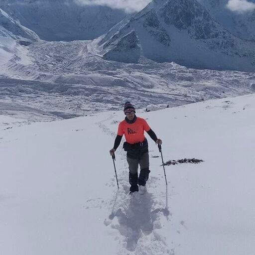 Hiker in an orange shirt using trekking poles on a snowy mountain