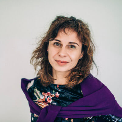Woman with curly brown hair and a purple wrap over a floral top