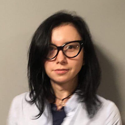 Woman with dark hair and large black glasses in a white jacket