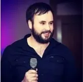 Bearded man in a dark shirt holding a microphone