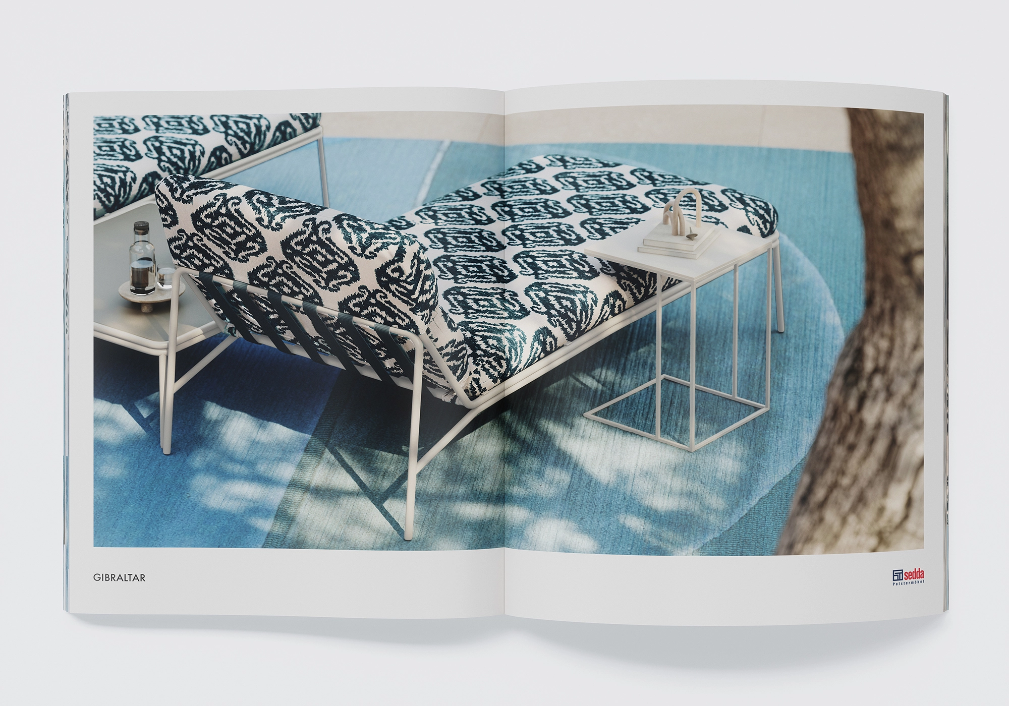 Outdoor lounger "Gibraltar" by Sedda with blue and white patterned cushions on a blue carpet, side table - detail.