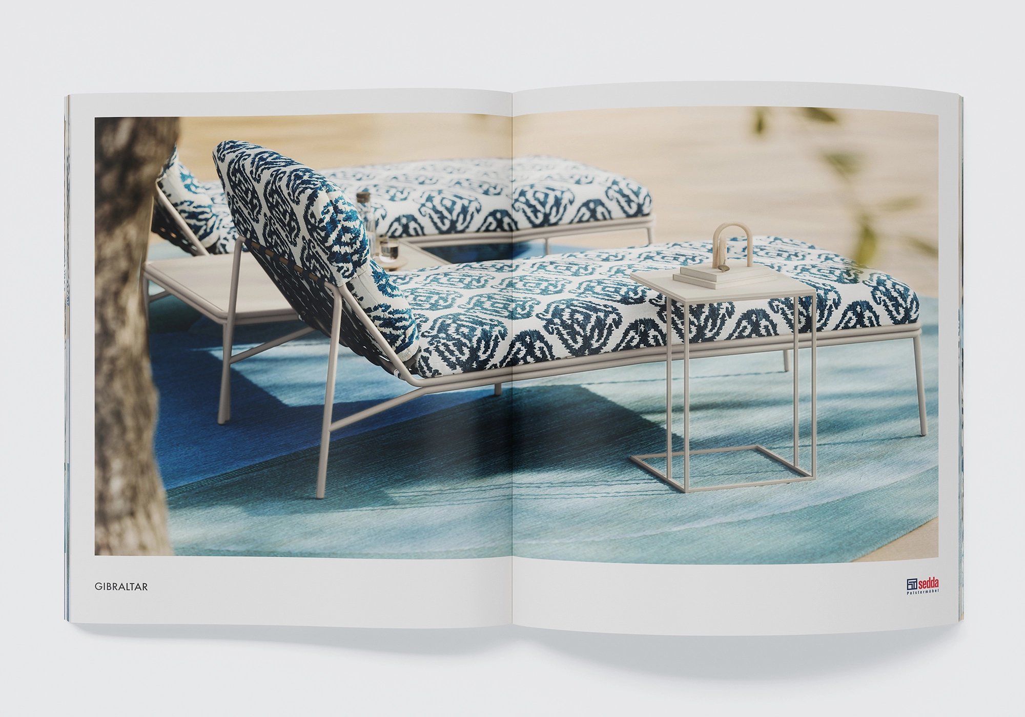 "Gibraltar" chaise longue from Sedda with graphic patterned fabric and slim frame, side table on blue outdoor rug.