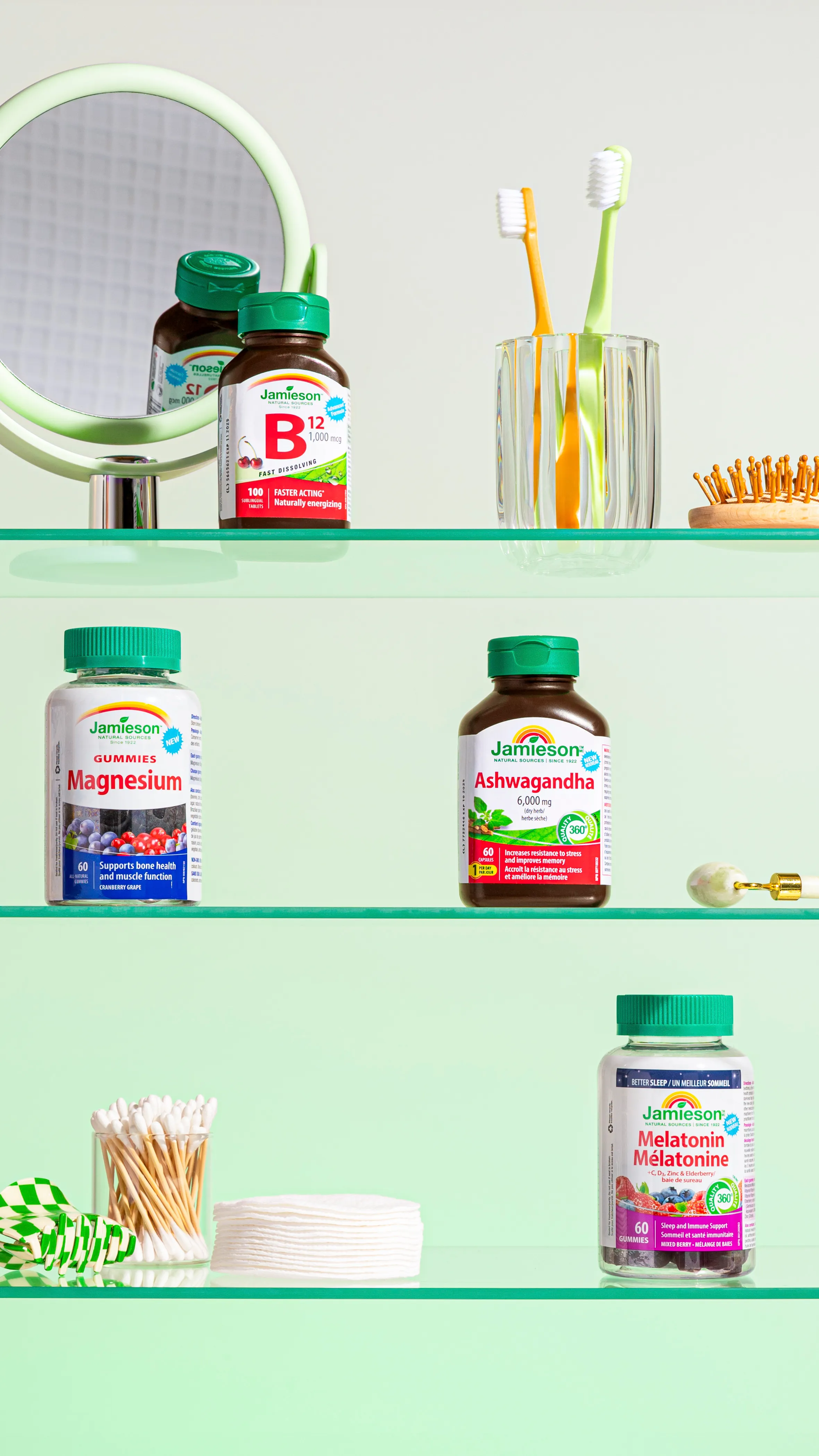 Three shelves with Jamieson vitamin bottles, a round mirror, two toothbrushes in a glass, cotton swabs, and cotton pads on a light green background.