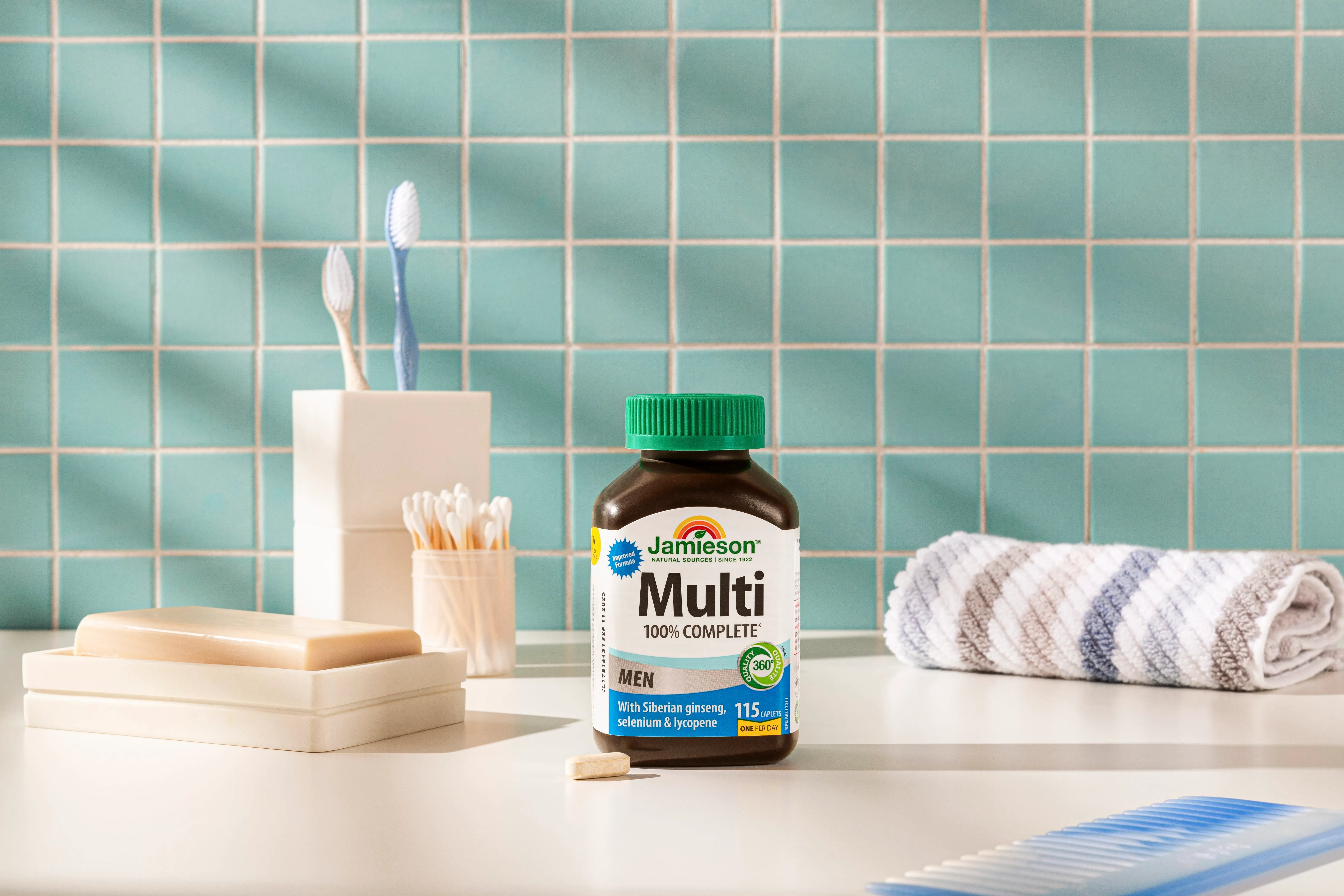 Jamieson Multi 100% Complete men's multivitamin bottle on bathroom counter with soap, toothbrushes, cotton swabs, towel, and comb.