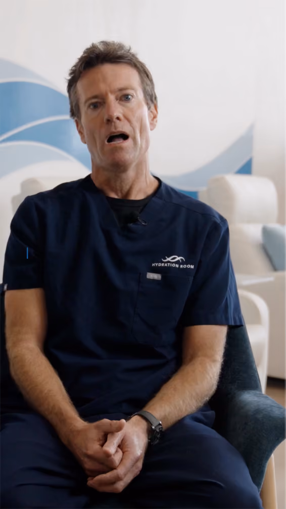 Man in navy blue medical scrubs sitting in a chair with hands clasped, speaking.