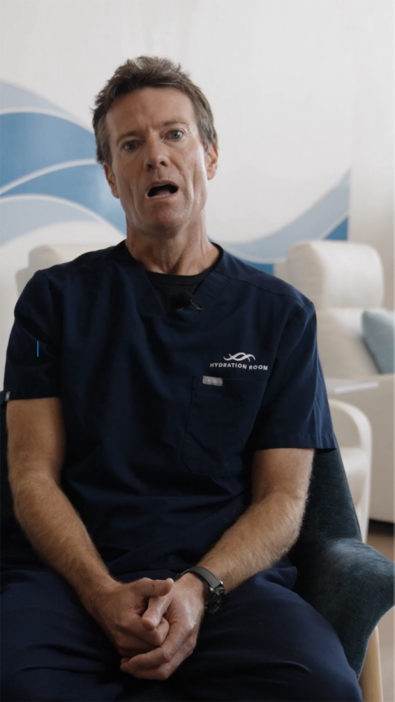 Man in navy blue medical scrubs sitting in a chair with hands clasped, speaking.