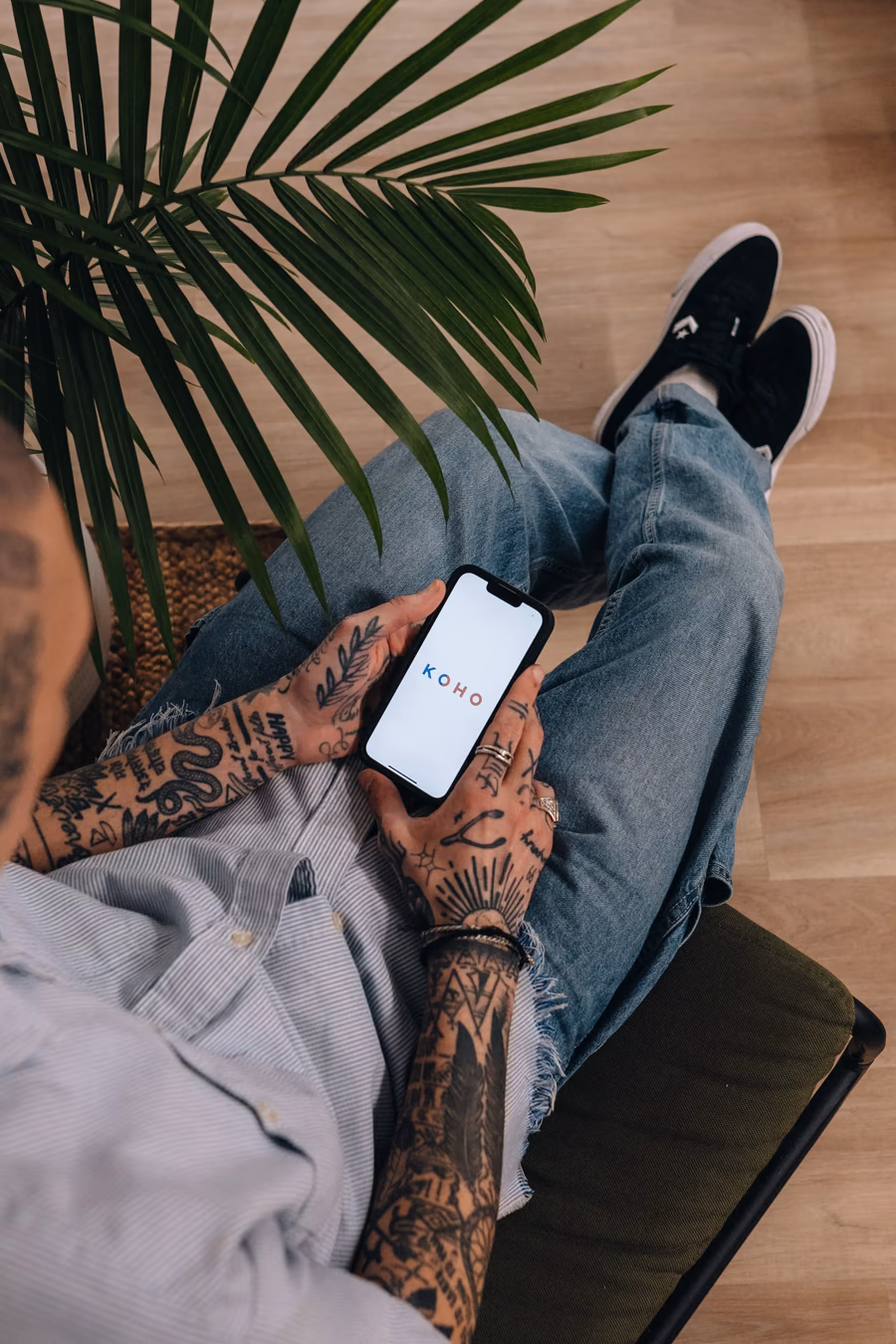 A man with tattoos and a blue shirt holding a phone.