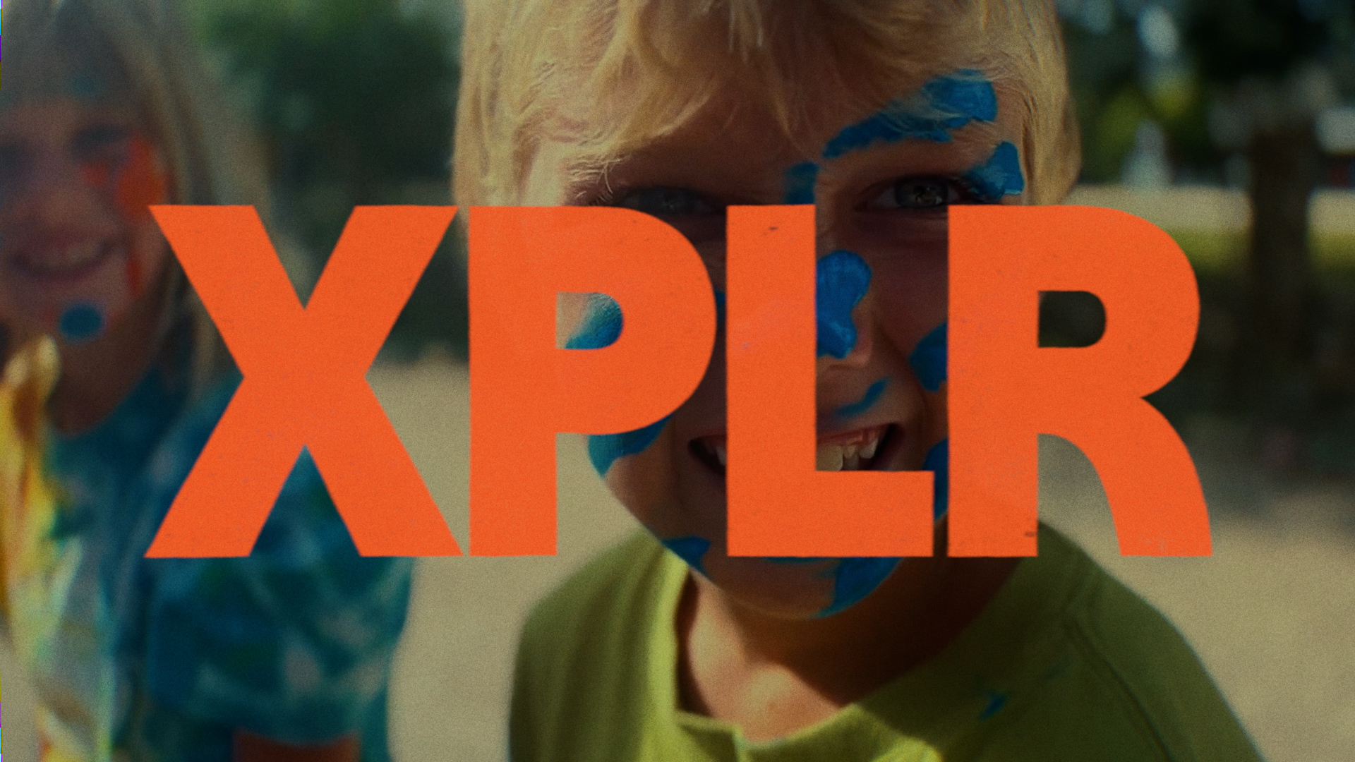 A young camper smiling and enjoying the sunny day with trees and greenery in the background.