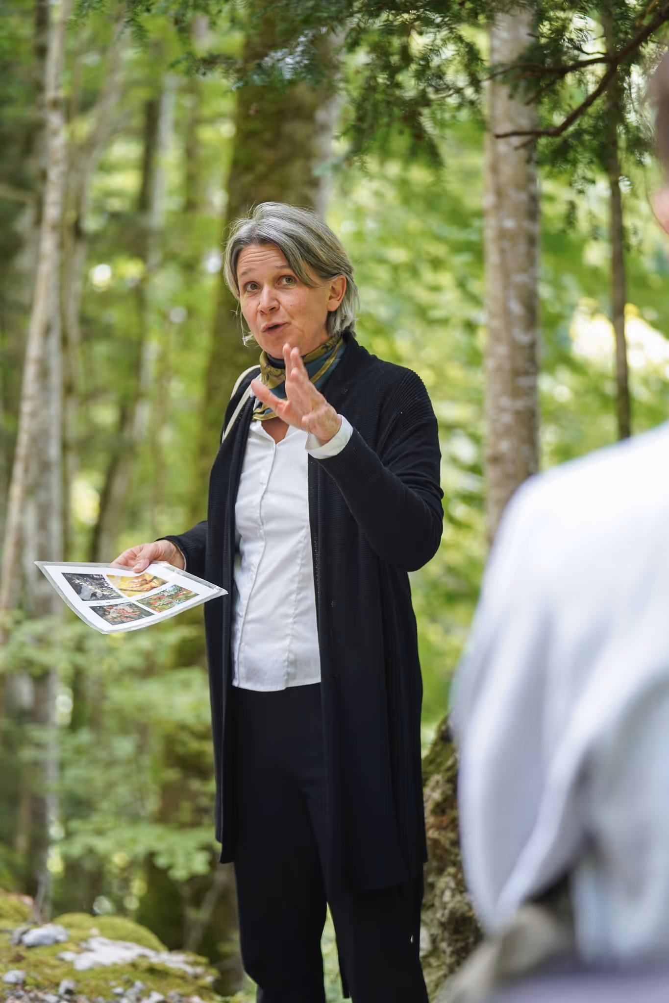 Diana Soldo spricht im Wald und hält ein Foto mit mehreren Bildern in der Hand.