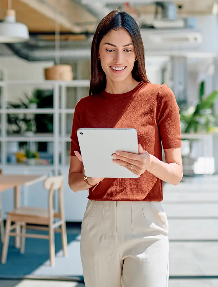 Lächelnde Frau steht mit einem Tablet in der Hand in einem hellen, modernen Büro.
