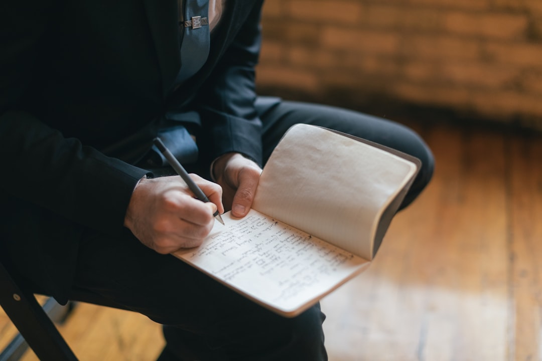 Person writing in a notebook with a pen.