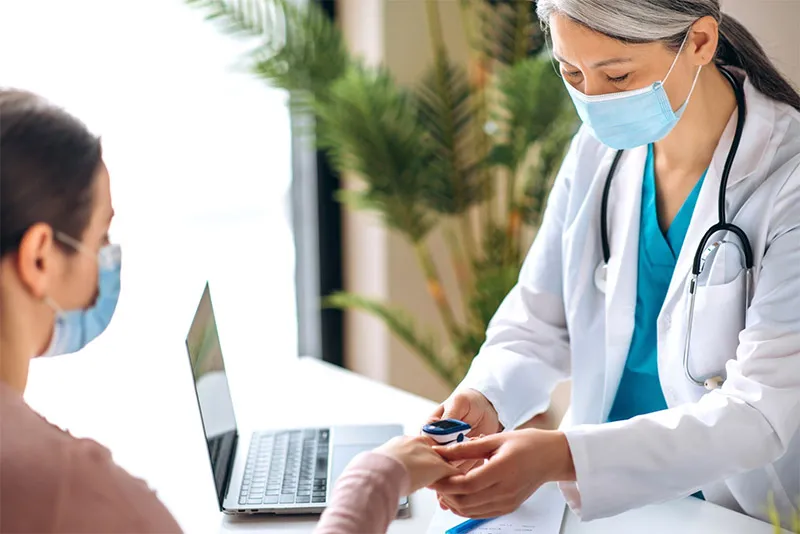 Doctor with face mask on checking the blood pressure of a patient