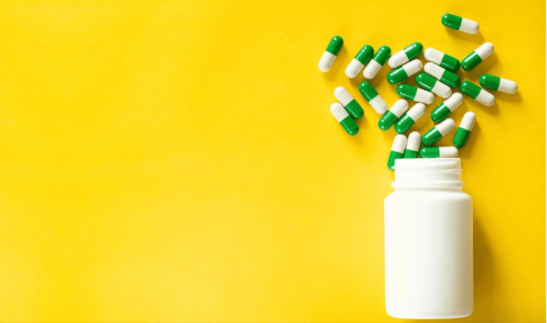Pills spilling out of a container on a yellow background