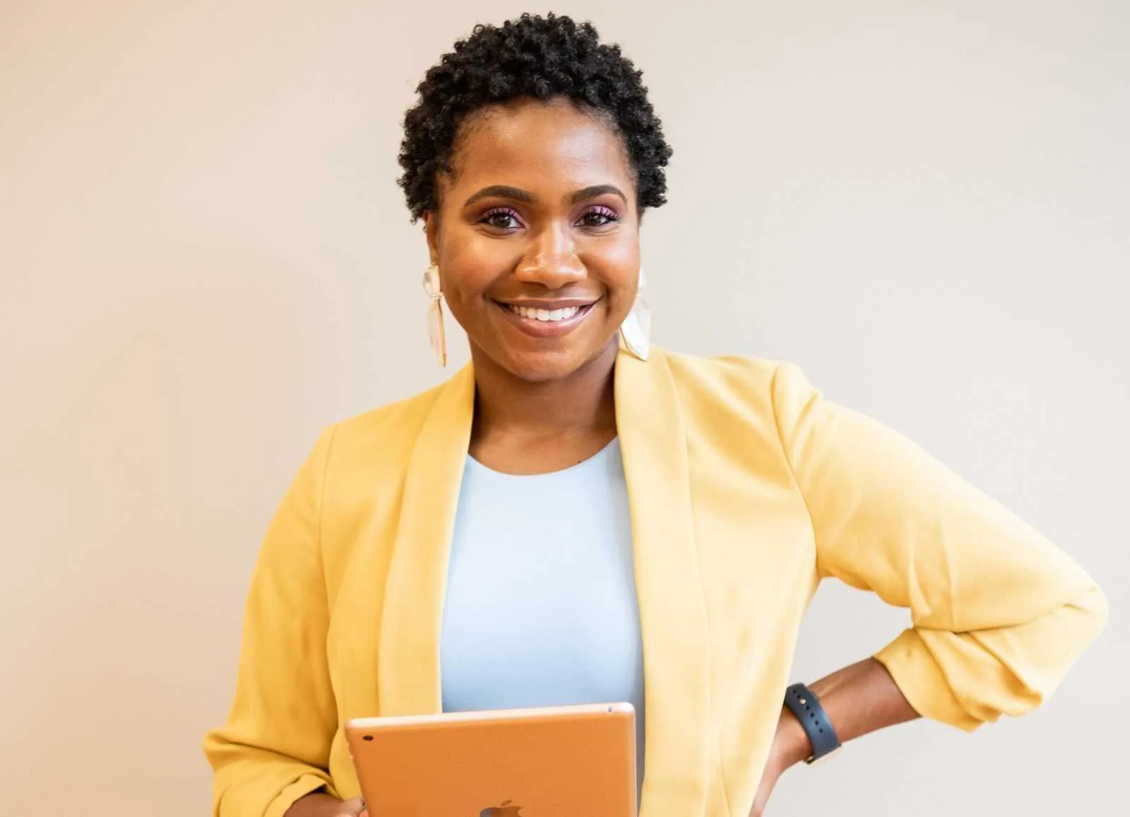 Woman in yellow blazer smiling and holding an ipad