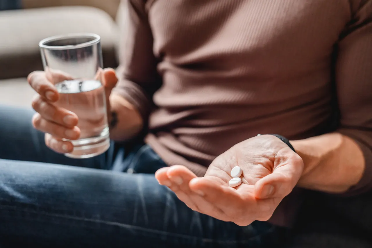 Close up of a person with a glass of water in one hand and medication in the other.