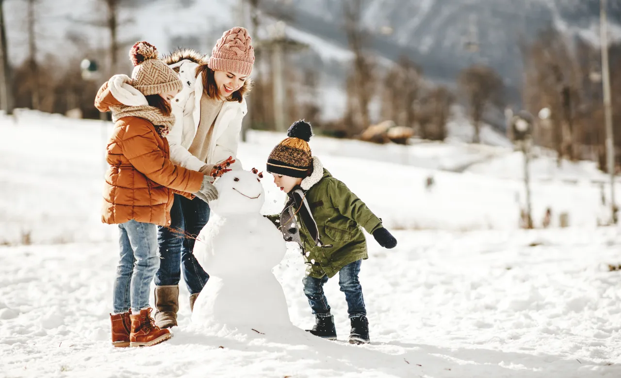 Two children and an adult women in winter wear playing in the snow