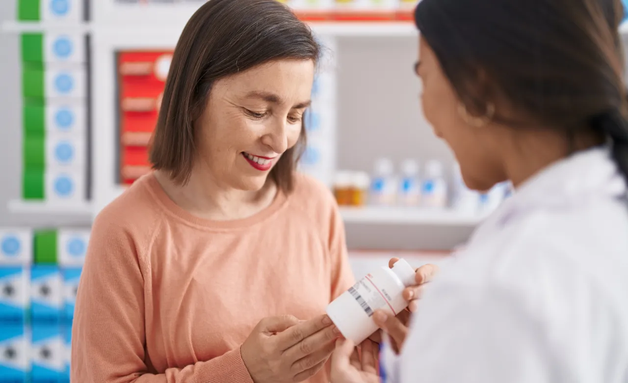 Woman looking at prescription bottle and talking with her pharmacist 