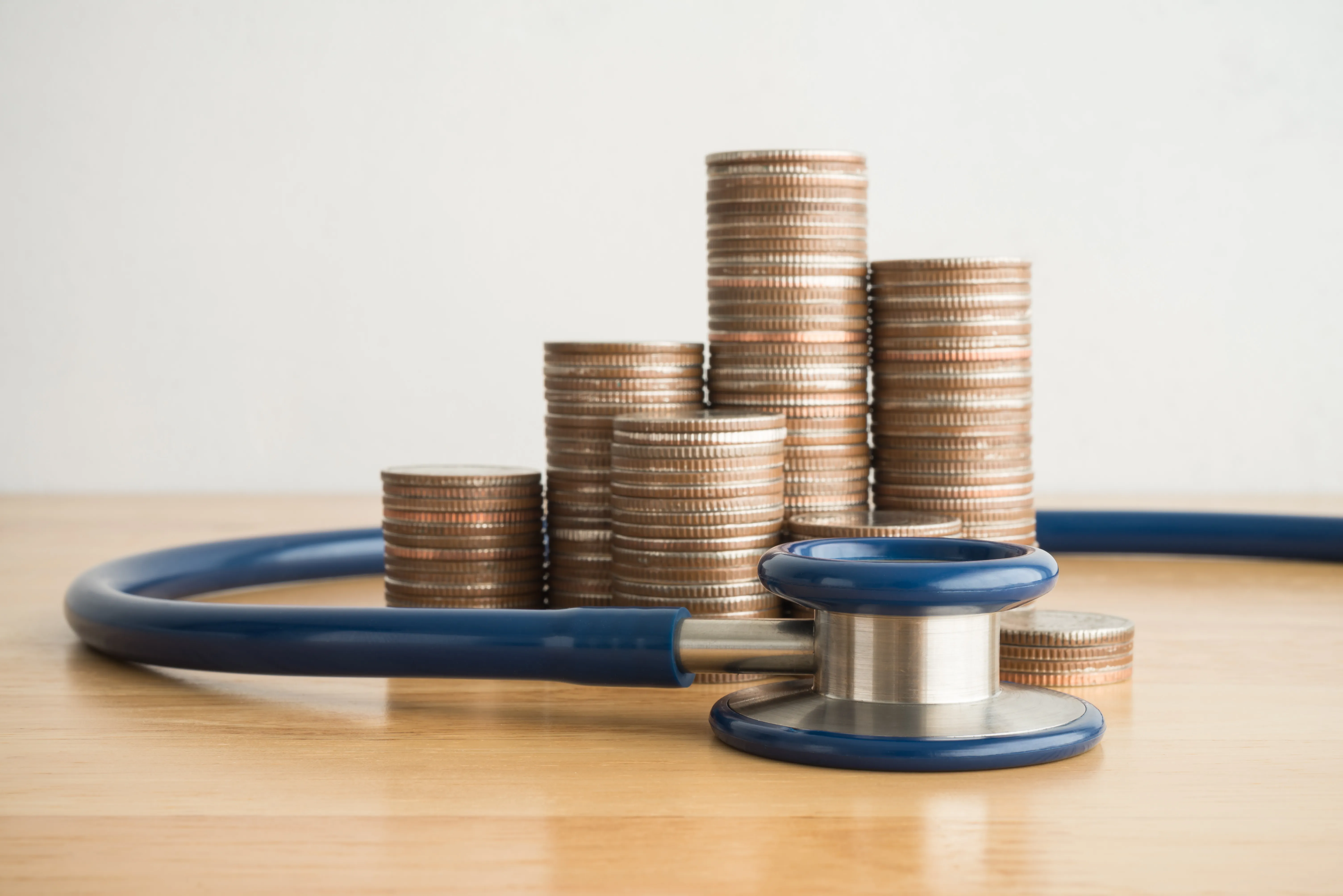 Coins stacked on desk enclosed by stethoscope