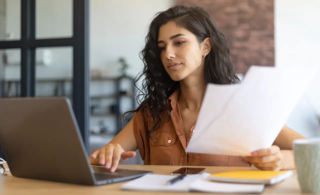 Woman at desk on computer holding papers