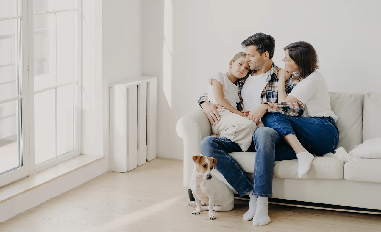 Family sitting on couch happily with their dog on the floor