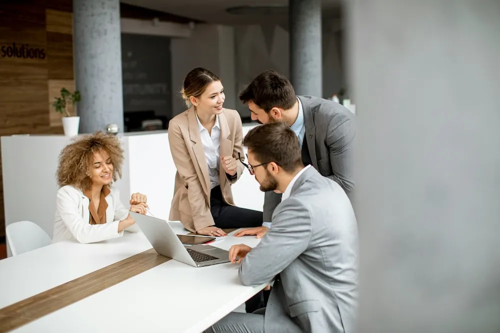 coworkers sitting and standing around long desk in conversation