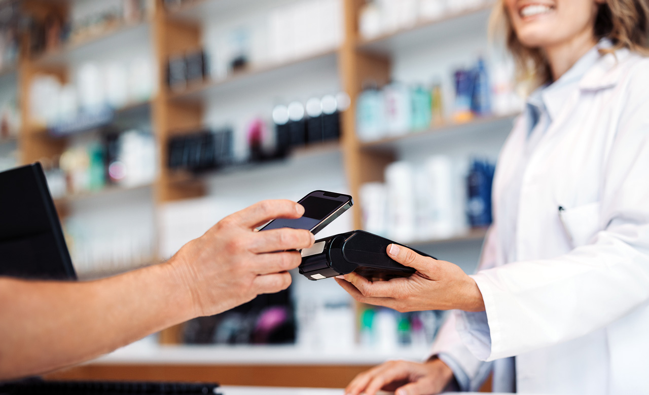 A customer using a smartphone for a contactless mobile payment at a pharmacy counter held by a pharmacist