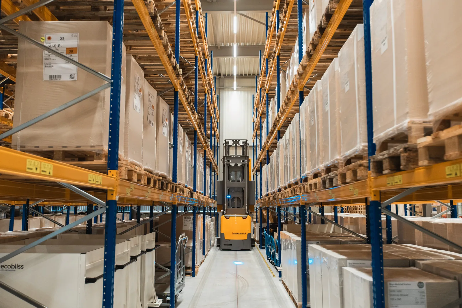 Wide view down a warehouse aisle between tall pallet racks full of packed goods