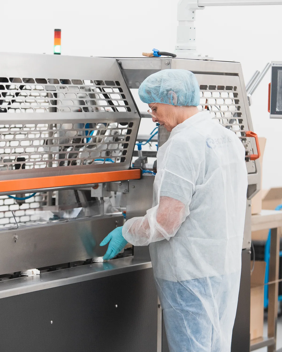 Operator in hairnet working at a stainless steel packaging machine with control panel